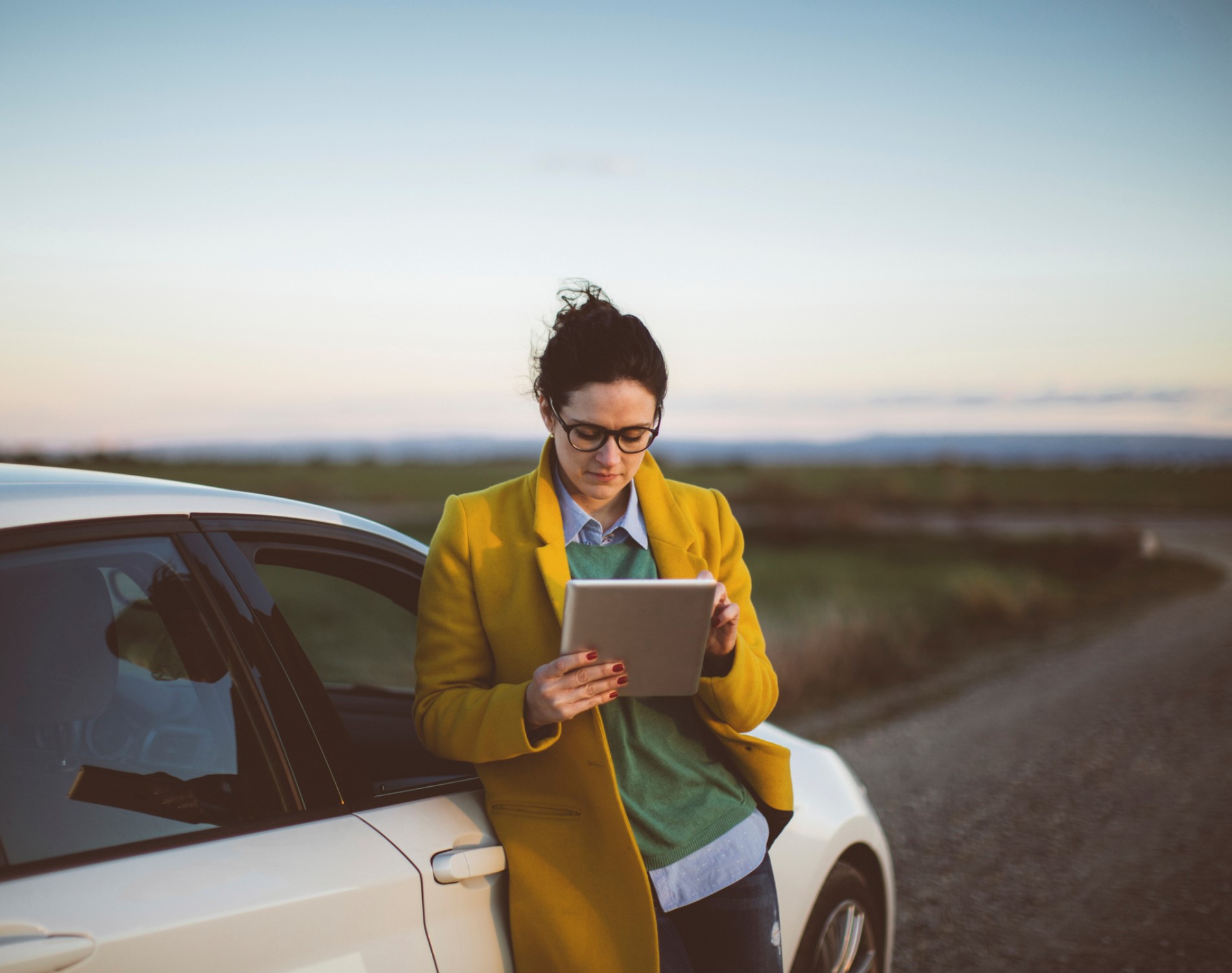 Woman on tablet leaning on car